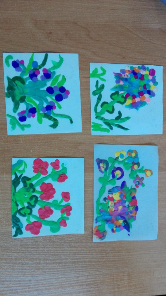 Na zdjęciu są cztery kartki z namalowanymi kwiatami. Łodygi są zielone i długie, płatki są kolorowymi plamami pozostawionymi po pędzlu
