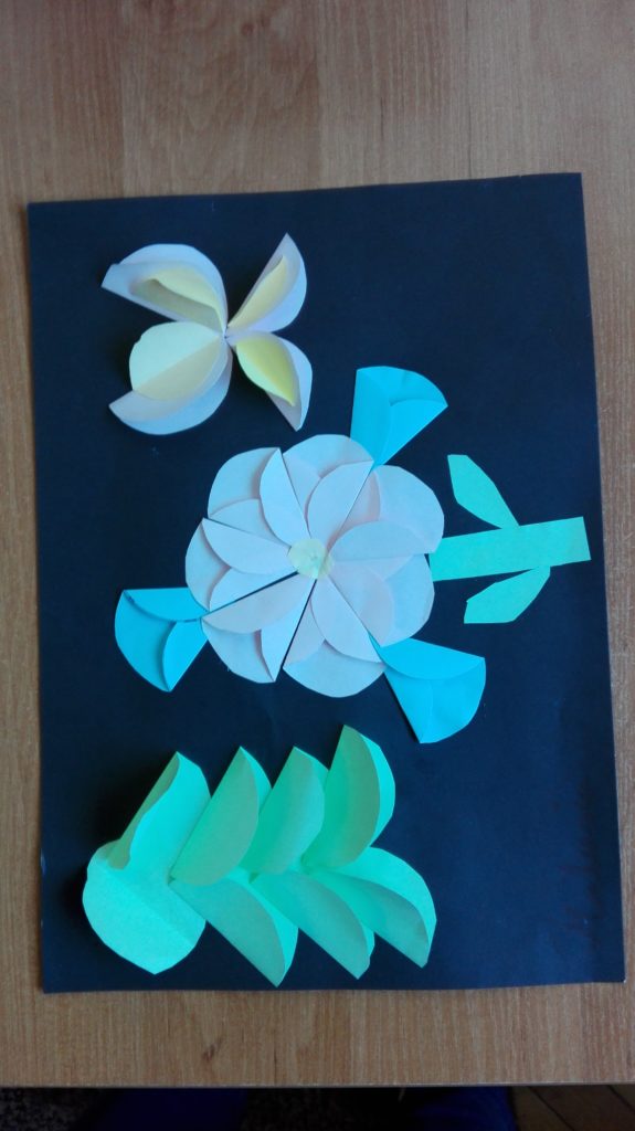 Na karce są kwiaty, których płatki są zrobione z przyklejonych kawałków papieru. Kwiaty wystają ponad płaszczyznę kartki